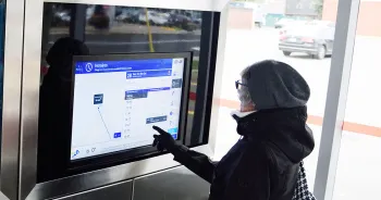 Une femme consulte l'horaire de son parcours sur un écran dans un arrêt de bus.